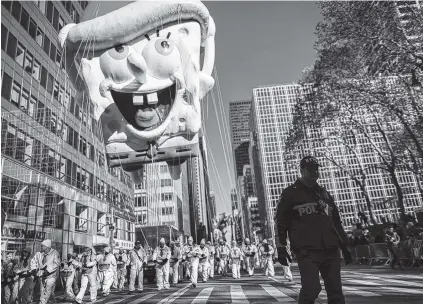  ?? THE ASSOCIATED PRESS ?? A New York City police officer, right, marches down Sixth Avenue ahead of a SpongeBob SquarePant­s balloon during the Thanksgivi­ng Day parade in New York on Thursday.