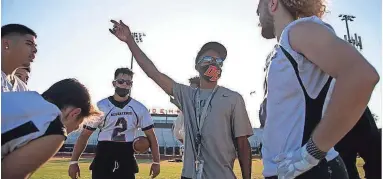  ?? MEG POTTER/ARIZONA REPUBLIC ?? Desert Edge football coach Mark Carter, middle, discusses practice drills with quarterbac­k Adryan Lara (2) and other players during a spring practice at Desert Edge High School on Tuesday.