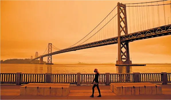  ??  ?? A woman walks along the Embarcader­o under an orange smokefille­d sky in San Francisco