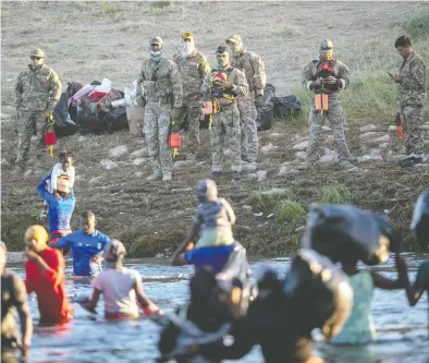  ?? JOHN MOORE / GETTY IMAGES ?? U.S. Border Patrol agents watch as Haitian families cross the Rio Grande from Mexico into Texas on Thursday after Mexican immigratio­n officials began an operation at a small migrant camp on the Mexican side of the river.