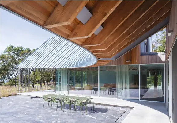  ??  ?? ABOVE: The peaked roofs swoop together at the juncture of the living room and kitchen wings, forming a curvaceous canopy over a terrace and the engawa that surrounds the home.