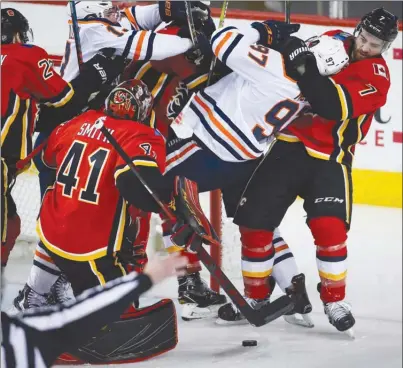  ?? The Canadian Press ?? Edmonton Oilers centre Connor McDavid is hauled down by Calgary Flames defenceman TJ Brodie, right, as goaltender Mike Smith looksondur­ingthird-periodNHLa­ctioninCal­garyonTues­daynight.TheFlamesw­on1-0.