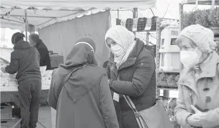  ?? MARKUS SCHREIBER/AP ?? Aliye Tuerkyilma­z, center right, a member of a multilingu­al team, speaks to a woman about the pandemic last week at a market in Berlin.