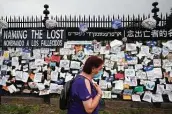  ?? Mark Lennihan / Associated Press ?? A woman passes a fence outside Brooklyn's Green-Wood Cemetery adorned with tributes to victims of COVID-19.