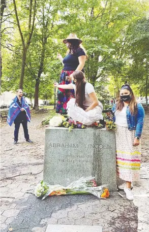  ?? KATIE HUNSBERGER ?? Trump supporter Brandon Doblie looks on as a group of Indigenous women — from left, Eva Angus, Michaila Taylor and Davineekah­t White Elk — pose on top of a podium in a Portland, Ore., park that used to hold a statue of Abraham Lincoln.
The monument was pulled down by protesters.