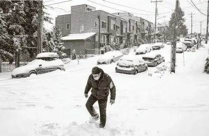  ?? Bettina Hansen / Associated Press ?? John Kramer walks down a street in the Seattle area Saturday as a winter storm blankets the Pacific Northwest with ice and snow, leaving hundreds of thousands of people without power and disrupting travel.