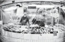  ?? ALVARO BARRIENTOS/AP ?? A masked worker stands inside a stall last week at a market in Pamplona, Spain.