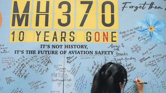  ?? AP ?? Una mujer escribe un mensaje en el muro de recuerdo a las víctimas del vuelo MH370, desapareci­do en mitad de la noche hace diez años