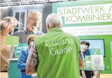  ?? FOTOS: FELIX KÄSTLE/DPA ?? Ein Corona-Guide spricht an einem Stand mit einer Besucherin. Er ist für die Einhaltung der Corona-Regeln in der Halle verantwort­lich.