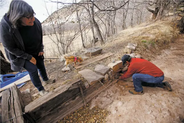  ?? PHOTOS BY LUIS SÁNCHEZ SATURNO/THE NEW MEXICAN ?? Virginia Johnson watches Friday as her husband, William Gonzales, cleans out the pipe that irrigates his field in Lourdes.