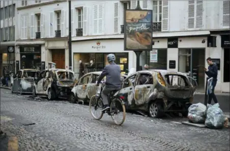  ?? KAMIL ZIHNIOGLU — THE ASSOCIATED PRESS ?? A man rides his bicycle past by charred cars, near the Arc de Triomphe, in Paris, Sunday. A protest against rising taxes and the high cost of living turned into a riot in the French capital Saturday, as activists caused widespread damage and tagged the Arc de Triomphe with multi-colored graffiti during clashes with police.