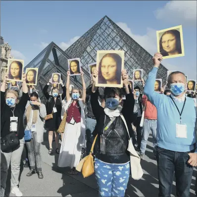  ?? PICTURE: GETTY IMAGES ?? ALL SMILES: Tourist guides hold reproducti­ons of the Mona Lisa outside the Louvre museum as it reopens its doors.