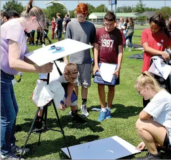  ?? Janelle Jessen/Herald-Leader ?? Middle school students watched as science teacher Donna Smith set up a solar viewer. The viewer consisted of a pair of binoculars on a tripod that reflected the image of the sun and moon on a piece of cardboard on the ground.