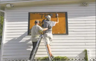  ?? Eric Hasert / Associated Press ?? Michael Boyle, left, helps keep Mike Russell steady as they work to cover a second-floor window of a historic 1905 house on Saturday in downtown Fort Pierce, Fla., while preparing for the arrival of Hurricane Isaias.