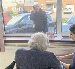  ??  ?? Resident Joan and her son talk on the phone through the window at Dene Holm Residentia­l Care Home in Northfleet while Margaret Smith enjoys St Patrick’s Day celebratio­ns