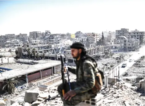  ??  ?? A fighter of the Syrian Democratic Forces (SDF) sits on guard on a rooftop in Raqqa on Saturday, after retaking the city from Daesh. (AFP)