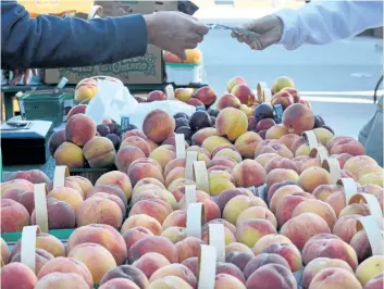  ?? JOE BARKOVICH/ SPECIAL TO POSTMEDIA NEWS ?? A market vendor makes a sale of juicy Niagara peaches at Welland Market Square.