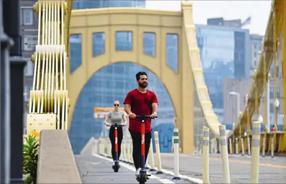  ?? Jack Myer/Post-Gazette ?? Pirates outfielder Ka’ai Tom, of Oahu, Hawaii, and Brittany Janicki, of Brooklyn, N.Y., cross the Roberto Clemente Bridge aboard Spin scooters. The electric scooters were introduced to the city in a pilot program two weeks ago.