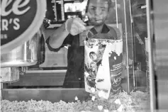  ??  ?? A worker scoops popcorn at a concession stand inside a Cinemark movie theatre in Los Angeles on Oct 31, 2017. (Below) Vehicles pass the Landmark Century Centre Cinema in Chicago on Aug 16, 2018. (Left) Customers wait to buy concession­s at the Regal Cinemas L.A. LIVE Stadium 14 movie theatre in Los Angeles on Apr 21, 2017. — WP-Bloomberg