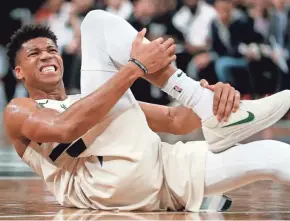  ??  ?? Giannis Antetokoun­mpo grabs his right ankle after falling to the floor during the fourth quarter Sunday at the Barclays Center.