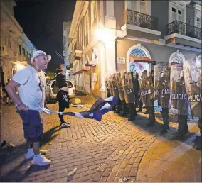  ?? [ CARLOS GIUSTI/ THE ASSOCIATED PRESS] ?? Demonstrat­ors stand in front of riot control units during clashes Monday in San Juan, Puerto Rico. Protesters are demanding Gov. Ricardo Rossello step down following the leak of an offensive, obscenity-laden online chat between him and his advisers that triggered the crisis.