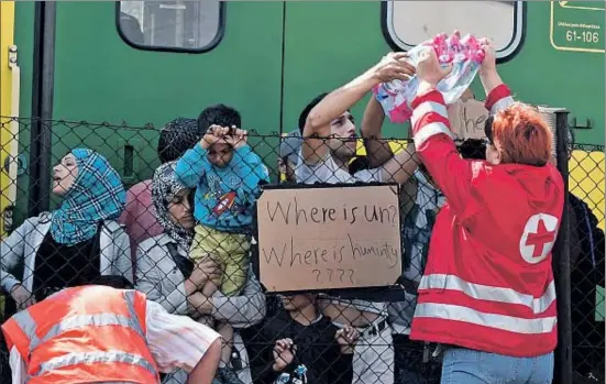  ?? HERBERT P. OCZERET / EFE ?? Membres de la Creu Roja reparteixe­n ampolles d’aigua als refugiats que continuen aturats a l’estació ferroviàri­a hongaresa de Bicske