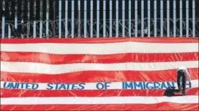  ?? REUTERS ?? A man writes on a large US flag as part of a protest called 'United States of Immigrants', aimed to demand respect for the migrants, near a border wall in El Paso, Texas.