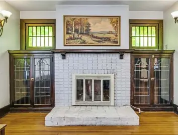  ??  ?? The working brick fireplace in the living room is flanked by built-in cabinets with leaded-glass doors and topped by stained-glass windows.