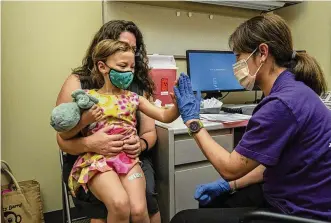  ?? DAVID RYDER/GETTY IMAGES/TNS ?? Nora Burlingame, 3, sits on the lap of her mother, Dina Burlingame, and gets a high five from nurse Luann Majeed after receiving her first dose of the Pfizer COVID-19 vaccinatio­n at UW Medical Center - Roosevelt on June 21, 2022, in Seattle, Washington.