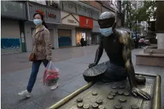  ?? AP Photo/Ng Han Guan ?? ■ A resident walks through a partially closed retail street, with a bronze statue covered with a face mask, on April 13 in Wuhan, China. Chinese leaders have reopened factories and shops in an effort to revive the economy, but the consumers whose spending propels most of China’s growth have been slow to return to shopping malls and auto dealership­s.