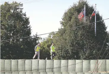  ??  ?? Workers walk across a flood wall made of Hesco barriers near the flood-swollen Cedar River in Cedar Rapids, Iowa.