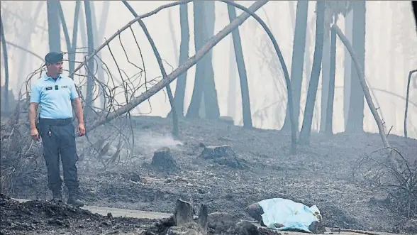  ?? MIGUEL A. LOPES / EFE ?? Un policía nacional custodia el cuerpo de unos de los fallecidos en el incendio, junto a la carretera hacia Pedrógão Grande