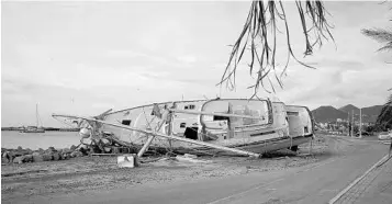  ?? PHOTOS BY HELENE VALENZUELA/AFP/GETTY IMAGES ?? Above, a boat sits on land Thursday in Marigot on the French Caribbean island of Saint Martin, after it was hit by Hurricane Irma. Below left, a resident cleans debris at his Marigot home, and a dog walks by a boat on the island, below right.