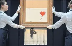  ??  ?? Sotheby’s employees pose with Banksy’s, Love Is In The Bin.