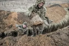  ?? Tyler Hicks/The New York Times ?? Ukrainian soldiers use buckets to clear mud from a trench position outside Toretsk, in the Donetsk province of eastern Ukraine on Saturday.