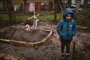  ?? Rodrigo Abd / Associated Press ?? In the courtyard of their house, Vlad Tanyuk, 6, stands near the grave of his mother Ira Tanyuk, who died because of starvation and stress due to the war, on the outskirts of Kyiv, Ukraine, on Monday.