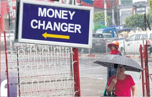  ??  ?? ABOVEA woman walks past a currency exchange centre in downtown Yangon.