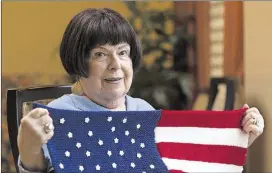  ?? CASEY SYKES / CASEY.SYKES@AJC.COM ?? Olive Ellner, 90, poses with an American flag lap quilt that she knitted at Huntcliff Summit, an independen­t living facility in Sandy Springs. When she sent off her first finished American flag quilt, she said it caused such an uproar at the VA...