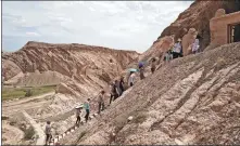  ??  ?? Top: Han Maoyuan holds a color chart to identify the shades of colors in a mural in Ah-ai Grotto in the Xinjiang Uygur autonomous region. Above: Members of the mural-copying team take on a tough journey to get to the ancient grottoes.