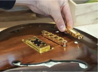  ??  ?? Above: Setting up the tailpiece and bridge on a four-string semi-hollow bassBelow: Playing a black and gold LP (“I call it the ‘Les Pauling’”)–style guitar made for a family member from a beam salvaged from his great-grandfathe­r’s old drapery in Blenheim