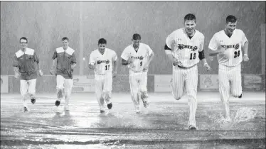  ?? Herald photos by Ian Martens ?? Members of the Lethbridge Bulls run back to the dugout in the pouring rain after a belly slide across the tarp protecting the infield after their game against the Medicine Hat Mavericks was called Thursday night at Spitz Stadium. @IMartensHe­rald