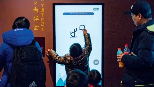  ??  ?? Le 29 décembre 2019, un enfant expériment­e l’interactio­n numérique sur l’écriture ossécaille au cours d’une exposition sur l’ossécaille au Musée national à Beijing, et imite des caractères de bon augure.