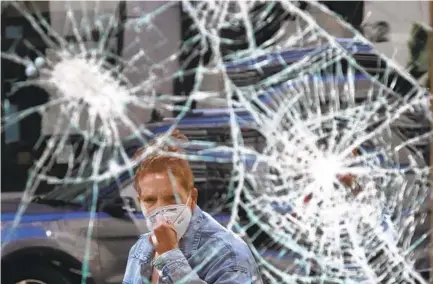  ?? ELISE AMENDOLA AP ?? A passerby looks at a smashed window Monday in Boston’s Downtown Crossing area. Rioting and looting have hit some shops hard.