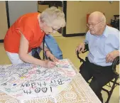  ??  ?? Shirley and Bill Gould sign the giant apron that served as a message book for well-wishers.