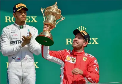  ?? AFP ?? Sebastian Vettel celebrates with his winner’s trophy as second-placed Lewis Hamilton looks on at Silverston­e. —
