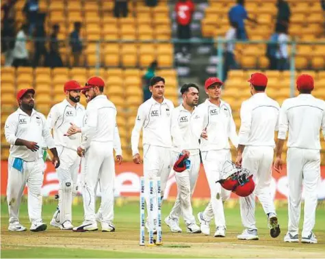  ?? AP ?? Afghanista­n players greet each other as they leave the ground at the end of the first day’s play of their debut Test against India.