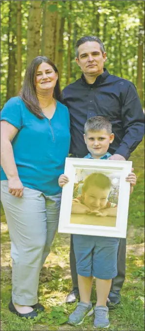 ?? (Evansville Courier & Press/Sam Owens) ?? Jamie, Andrew and 7-year-old Owen Dill stand with a framed photo of Oliver in their backyard on the west side of Evansville, Ind. The Dills’ 3-year-old son Oliver, also known as “Ollie,” died in 2019 after accidental­ly being forgotten in a car on the University of Southern Indiana campus.