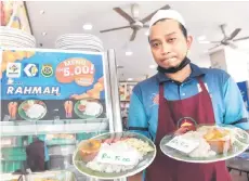  ?? — Bernama photo ?? A worker of Ali Maju Wisma Sri Rampai Restaurant in Kuala Lumpur showing the ‘Menu Rahmah’. The set menu, which offers rice, fish and a portion of vegetables, is priced at RM5.