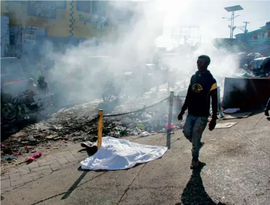  ?? CLARENS SIFFROY/AFP VIA GETTY IMAGES ?? A man walked past the body of a person who was killed by gang members in the street in Pétionvill­e, Haiti, on Monday.