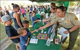  ?? Dan Watson/The Signal ?? L.A. County sheriff’s explorer Karen Jimenez, right, hands out stickers to children at the sheriff’s booth to kick off the National Night Out Against Crime at the Concerts in the Park event, which was held at Central Park in Saugus on Saturday.